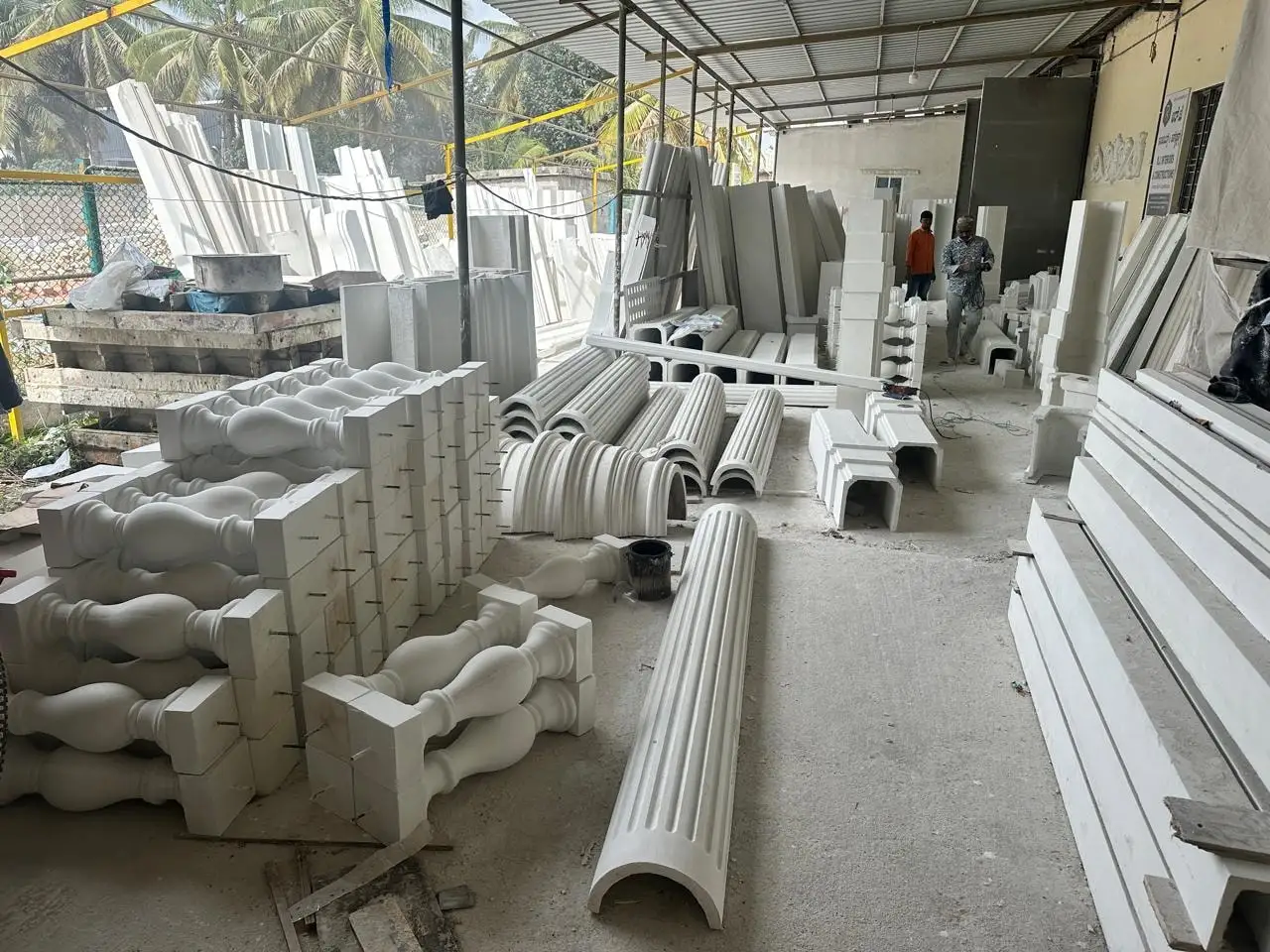 Finished white balusters, fluted column shells and cornice lengths stacked in the open yard of the unit