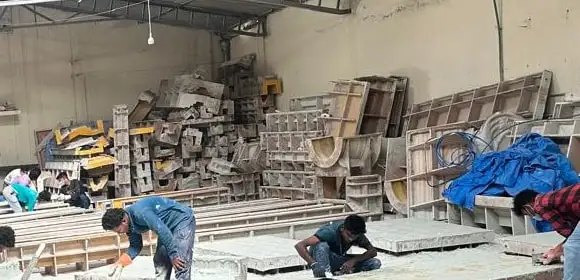 Moulds stacked at the back of the workshop hall, with workers finishing panels on tables in front